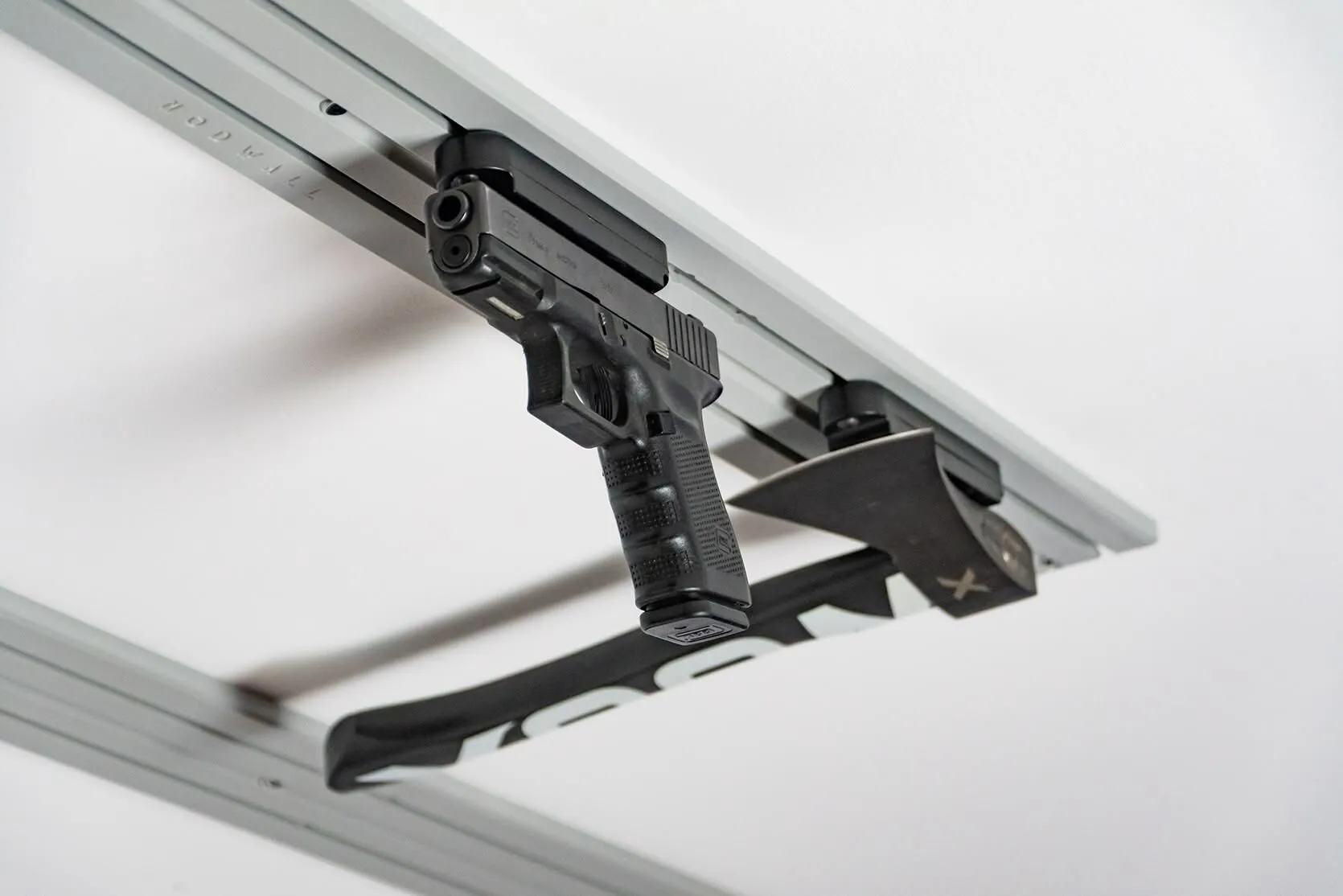 ModWall Ceiling Panel Strip (48″x4″) A handgun and a tactical axe are mounted using specialized modular mounts. This overhead configuration keeps defensive gear organized and accessible while remaining out of the way.