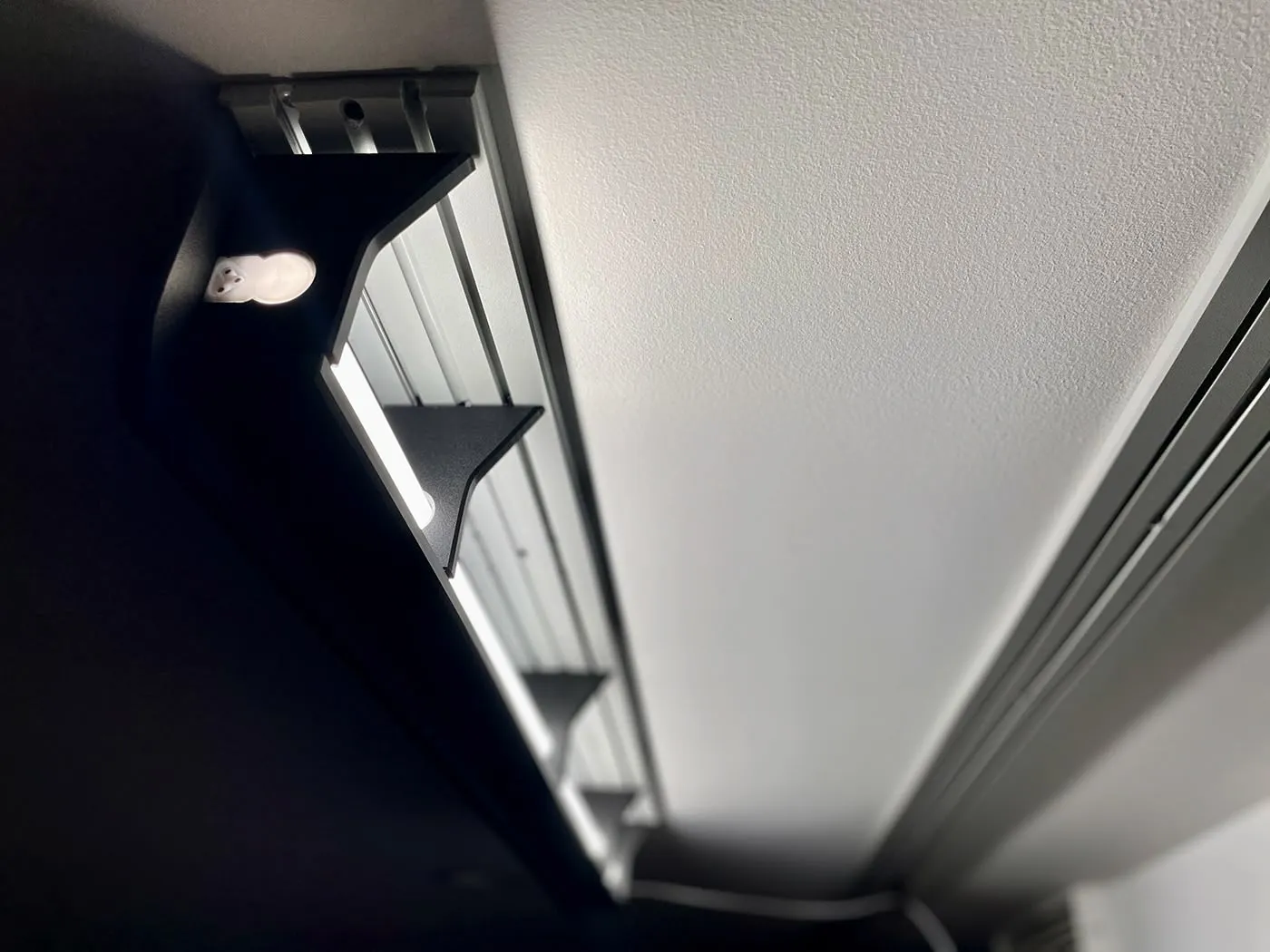 ModWall Ceiling Panel Strip (48″x4″) A close-up, low-angle view of a mounted, black LED light fixture on a white ceiling using the panel strip. The fixture provides bright, directed illumination, showcasing how the modular ceiling system can integrate lighting solutions for your gun room or workshop.