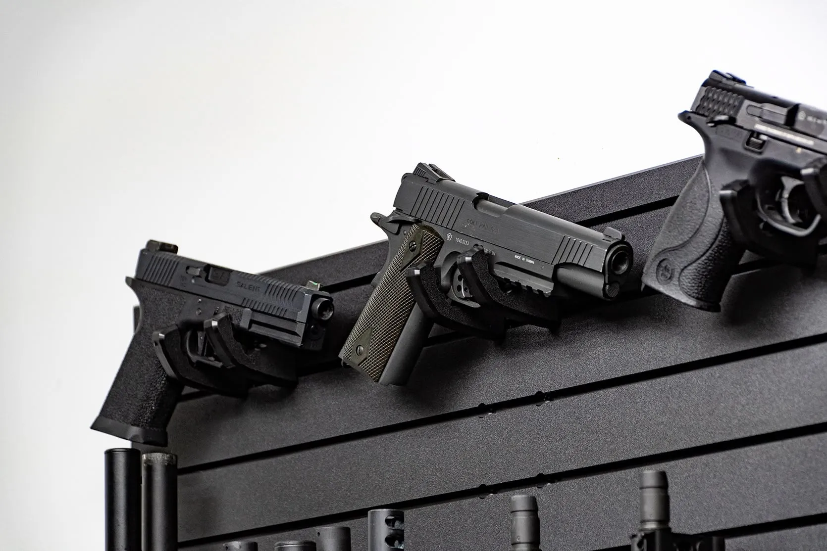 ModWall Compact 21 Gun Package Three handguns mounted at an angle on individual hangers against a black modular wall panel. This display shows how to keep multiple sidearms organized and ready for fast access in a home defense setup.