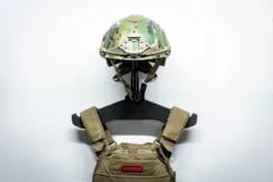 A camo tactical helmet and tactical vest hung on a heavy gear hanger mounted directly to a white wall.