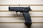 A black pistol with the barrel facing left mounted a tan gun wall system.