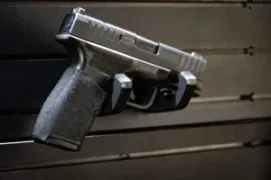 Wall mounted handgun rack securing a full size pistol on panel.