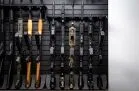 A high-density display of rifles and shotguns mounted vertically on a black modular wall panel. This layout organizes diverse firearms including AK-47s and AR-15s in a space-saving, professional configuration.