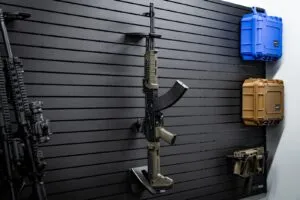 An angled side view of a rifle with a magazine inserted, mounted on a black slatwall system using the ModWall Vertical One Rifle Rack.
