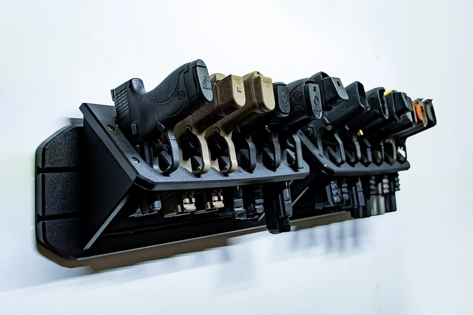 MidMod Panel A close-up, angled view of two black, wall-mounted storage racks holding multiple handguns against a plain white wall.