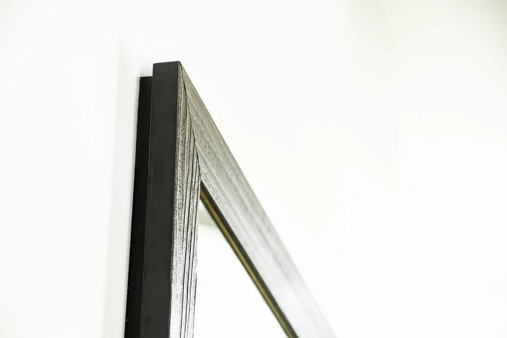 1450 Framed Concealment Mirror A close-up, angled view of the top corner of a dark, espresso-colored wood mirror frame showing grain texture and a black side profile.
