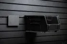 ModWall Rack Bin Set A black, square adapter plate attached to the panel beside a large black Uline storage container, which the container sits on.