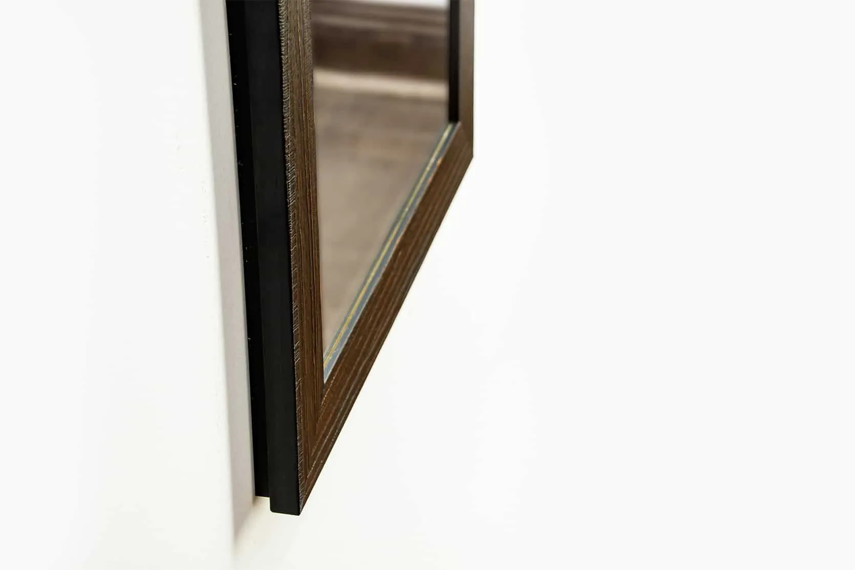 1450 Framed Concealment Mirror A close-up, angled view of the bottom corner of a dark, walnut-colored wood mirror frame mounted against a white wall.