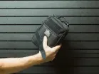 ModWall Strap Blocks A person unstrapping a small, compact black bag from a black modular wall panel.