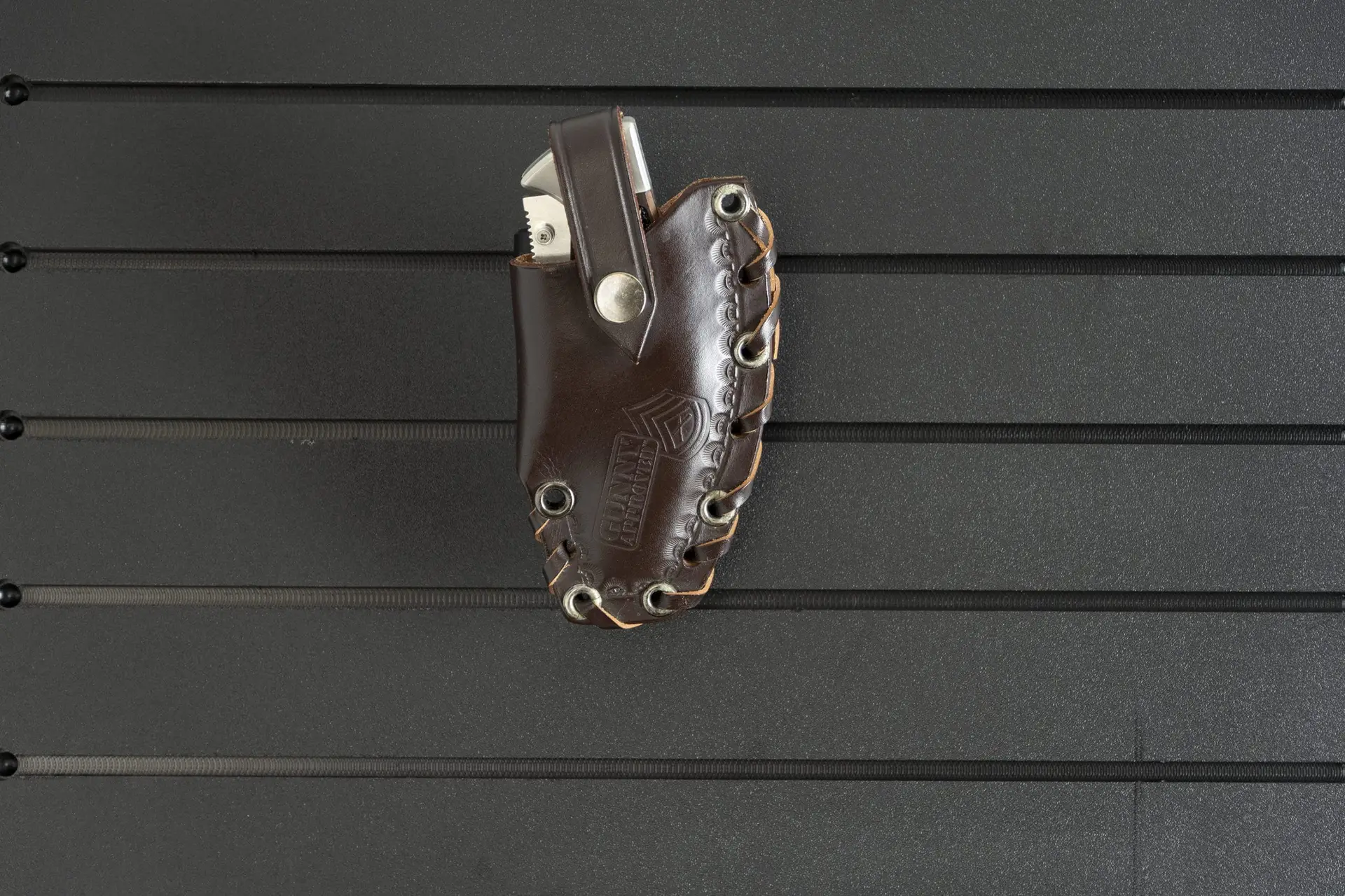 ModWall Tactical Belt Mount A dark brown knife pouch hung from the tactical belt wall mount against a black ModWall panel.
