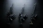 ModWall Sideways Vertical Rifle Rack Three different rifles hung by their magazines mounted on a black, gun wall panel.