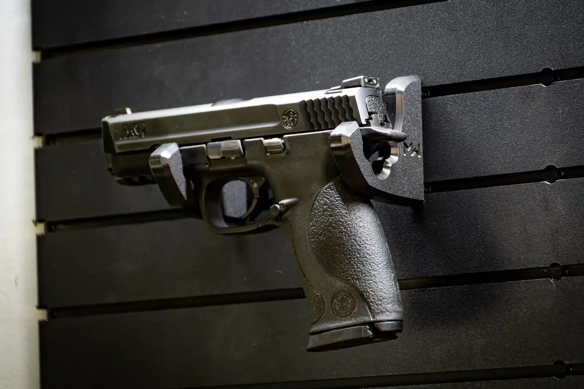 Wall mounted handgun rack securing a full size pistol on panel.