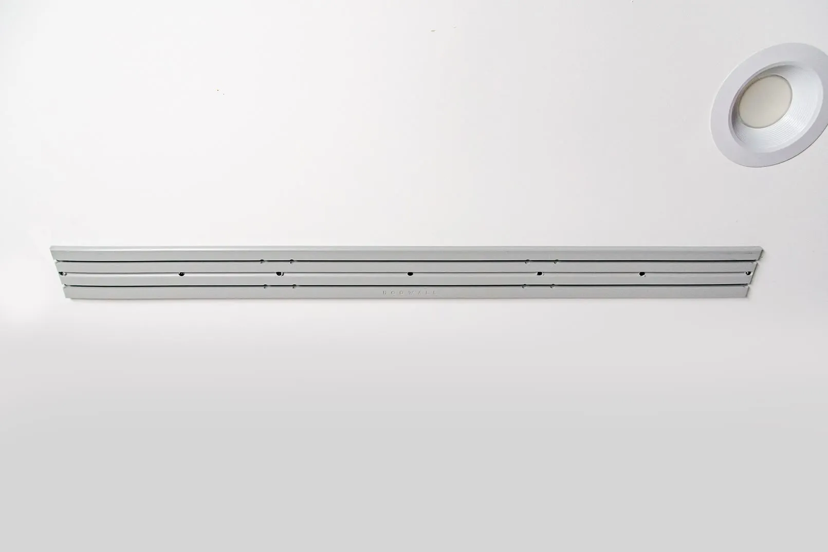 ModWall Ceiling Panel Strip (48″x4″) A 48-inch light grey ModWall Ceiling Panel Strip mounted horizontally on a white ceiling next to a recessed light, featuring modular slots for attaching storage accessories.