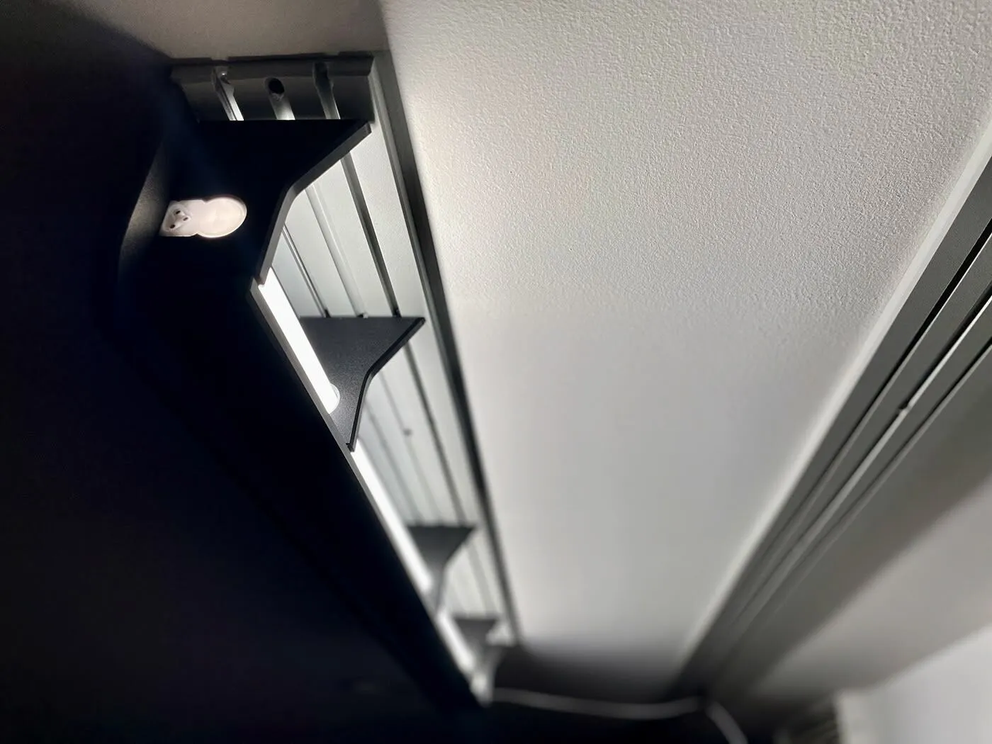 ModWall Ceiling Panel Strip (48″x4″) A close-up, low-angle view of a mounted, black LED light fixture on a white ceiling using the panel strip. The fixture provides bright, directed illumination, showcasing how the modular ceiling system can integrate lighting solutions for your gun room or workshop.