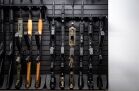 ModWall Compact 21 Gun Package A high-density display of rifles and shotguns mounted vertically on a black modular wall panel. This layout organizes diverse firearms including AK-47s and AR-15s in a space-saving, professional configuration.