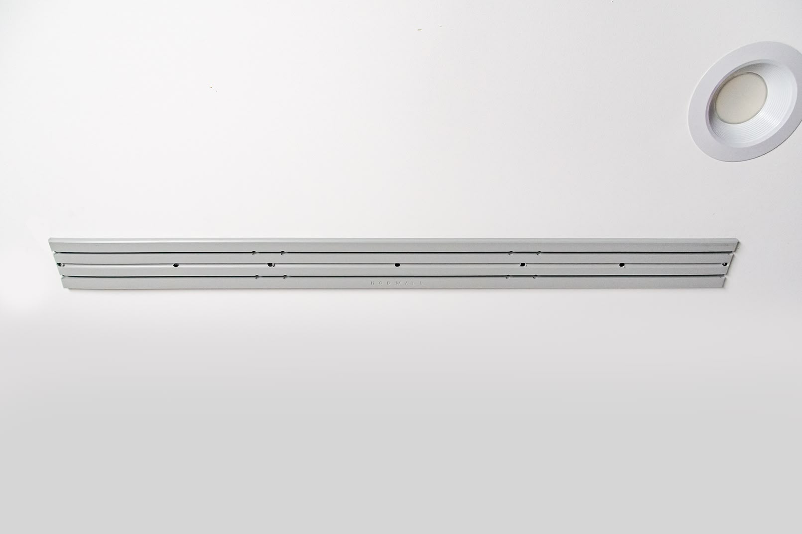 ModWall Ceiling Panel Strip (48″x4″) A 48-inch light grey ModWall Ceiling Panel Strip mounted horizontally on a white ceiling next to a recessed light, featuring modular slots for attaching storage accessories.