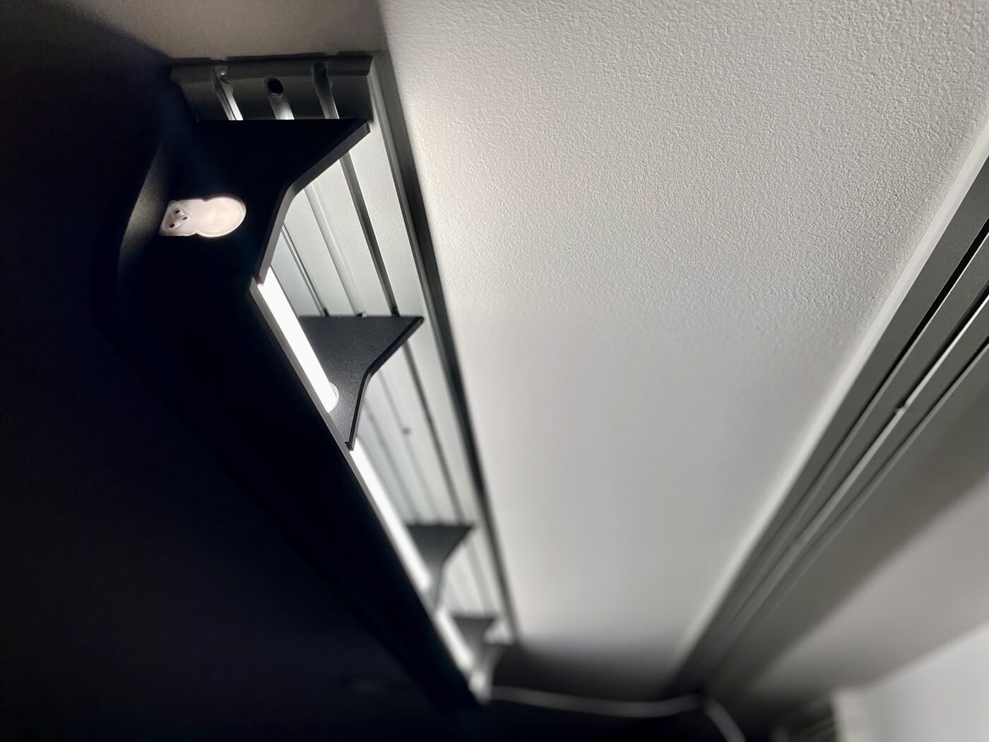 ModWall Ceiling Panel Strip (48″x4″) A close-up, low-angle view of a mounted, black LED light fixture on a white ceiling using the panel strip. The fixture provides bright, directed illumination, showcasing how the modular ceiling system can integrate lighting solutions for your gun room or workshop.