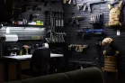 ModWall Panels (48″Wx22″H) A professional gun room corner featuring two walls covered in black ModWall panels. The setup organizes a wide array of equipment, including vertical rifle racks, horizontal mounts, pistols, magazines, and tactical gear like helmets and plate carriers next to a functional workspace.