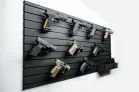 ModWall Panels (48″Wx22″H) A single panel pistol package mounted on a plain white wall, showcasing nine various handguns organized with individual mounts. The modular setup also includes a small shelf at the bottom right for storing magazines.