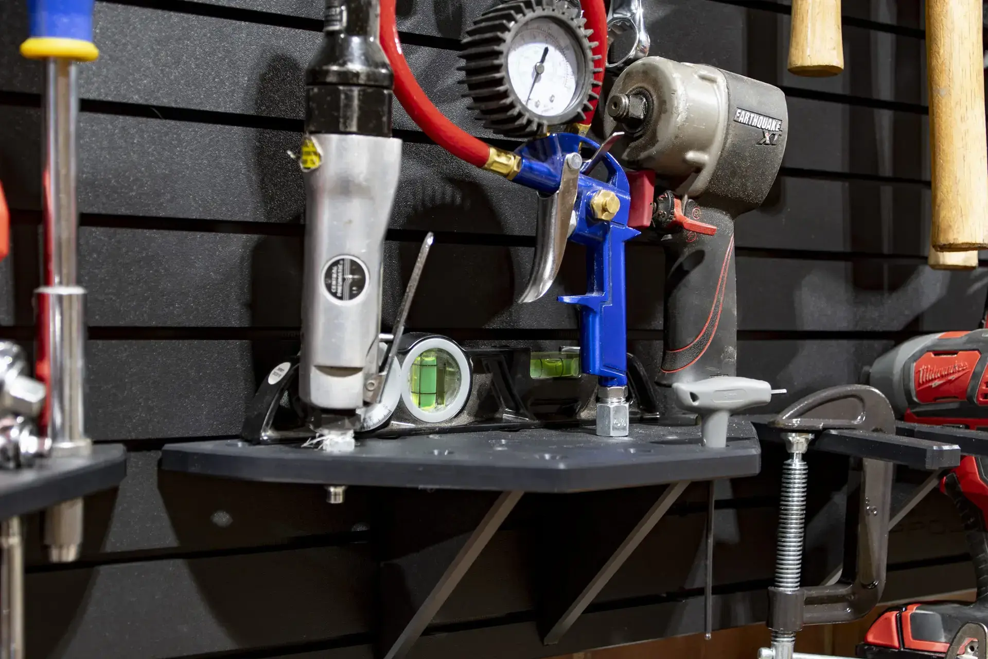 ModWall Air Tool Rack Air tool rack shelf holding an air grease gun, spray gun, impact wrench, and level on a black HDPE panel