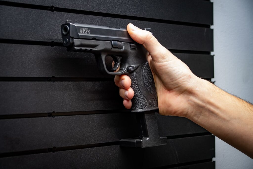 A black pistol being manually mounted on the ModWall pistol hanger with the barrel facing left against a black ModWall gun panel.