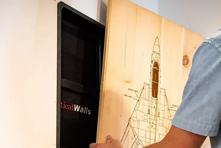 A person putting a piece of wooden art on the wall insert, providing concealment.