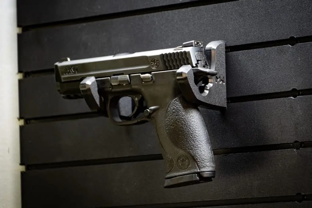 Wall mounted handgun rack securing a full size pistol on panel.