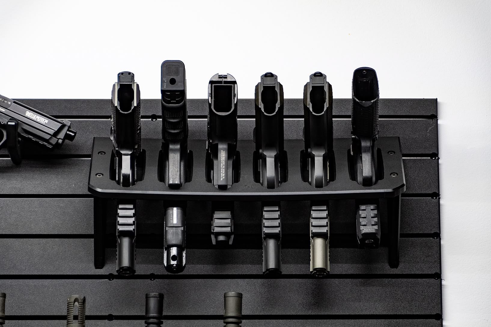 A top-down view of six handguns secured in a vertical rack on a black modular wall panel.