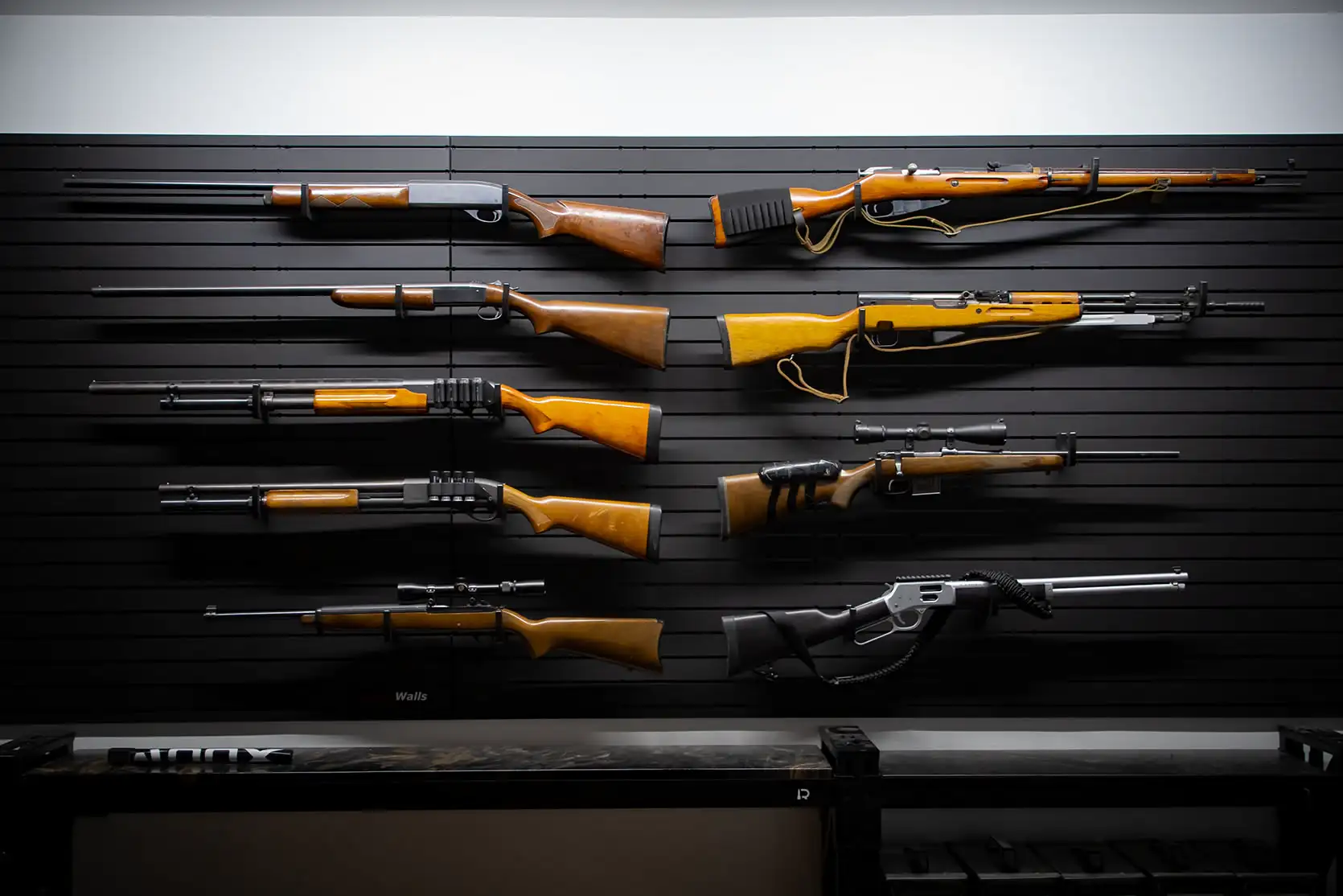 A large firearm collection featuring various shotguns and scoped long guns organized neatly on wall-mounted rifle racks.