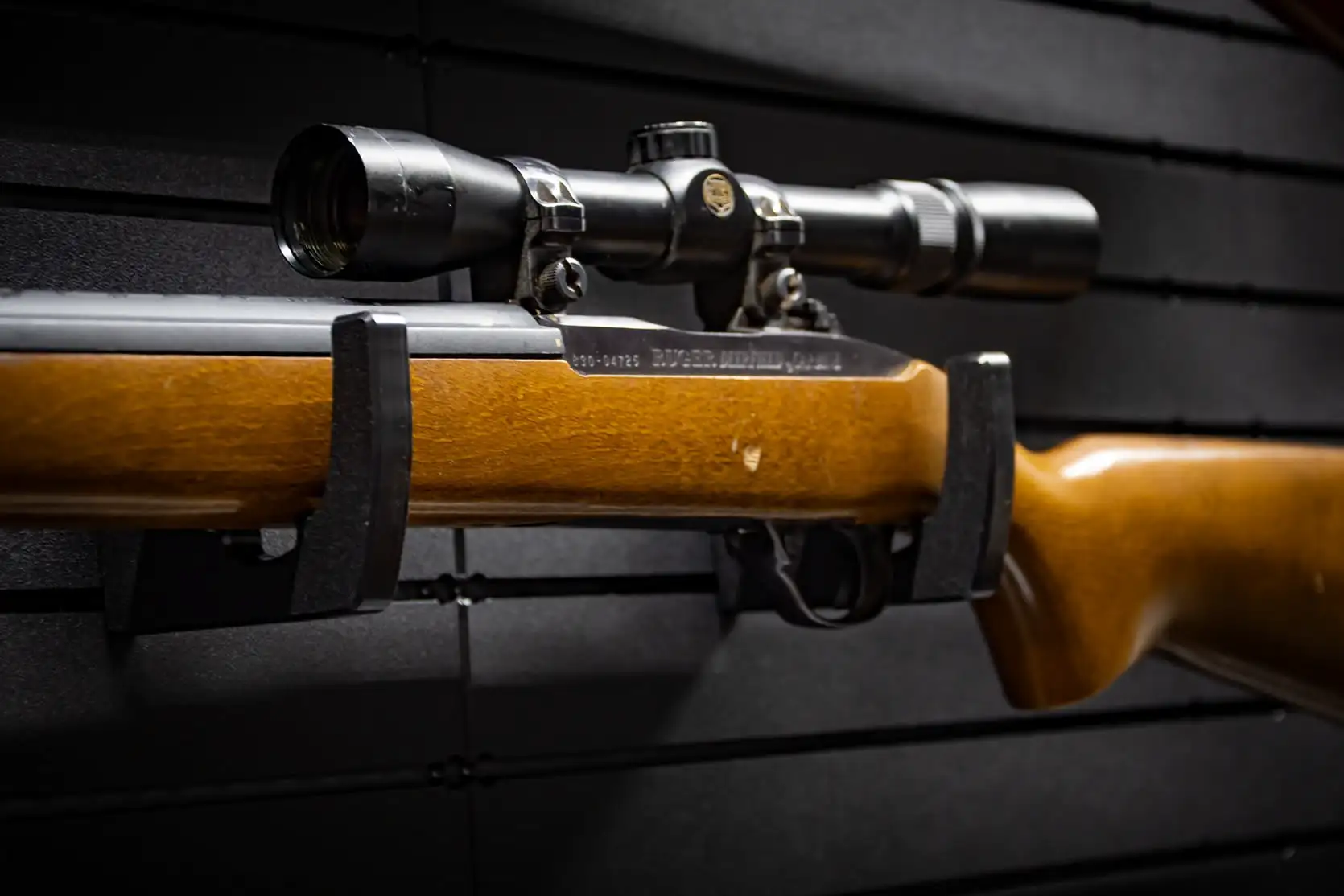 A scoped wood-stock rifle resting securely in a ModWall Horizontal Gun Racks hook attachment.