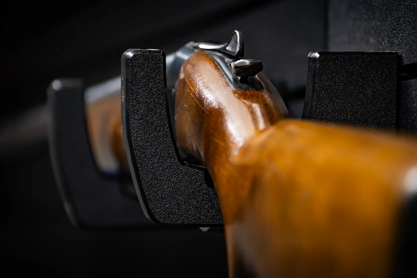 Close-up rear perspective of a polished wooden firearm stock cradled safely in protective HDPE wall hooks.
