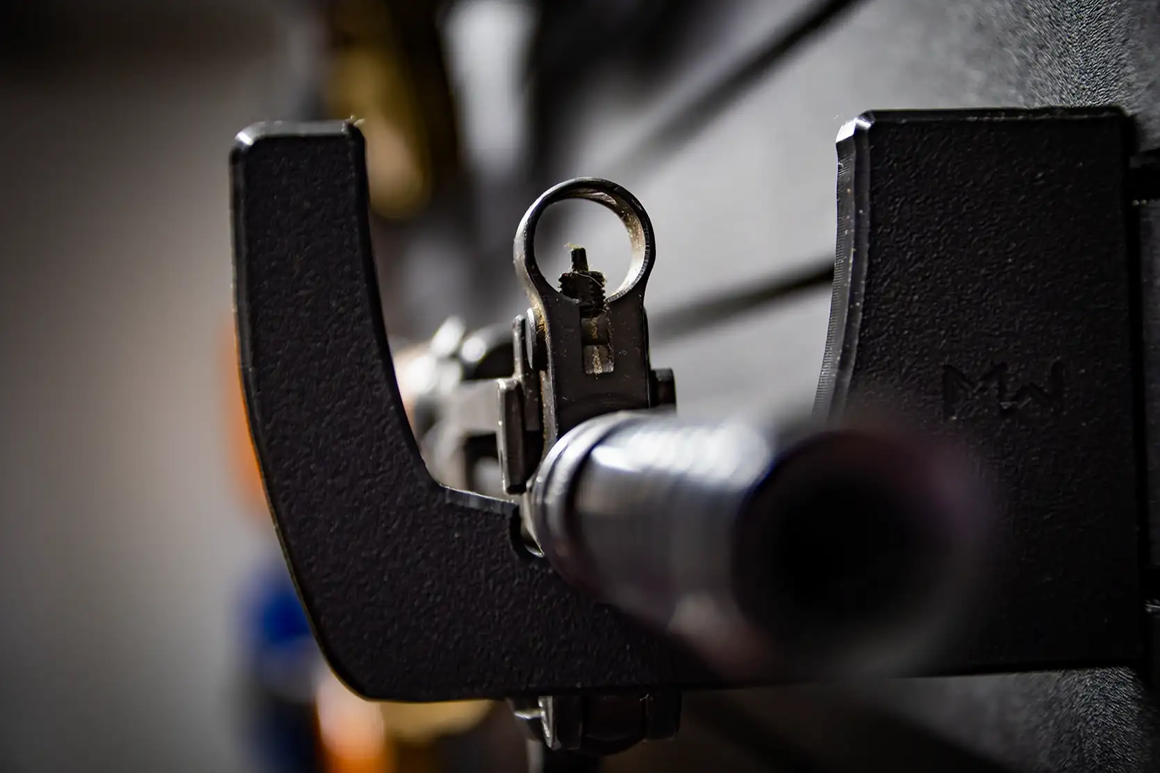 Looking down the barrel and front sight of a long gun supported by a black wall mount.