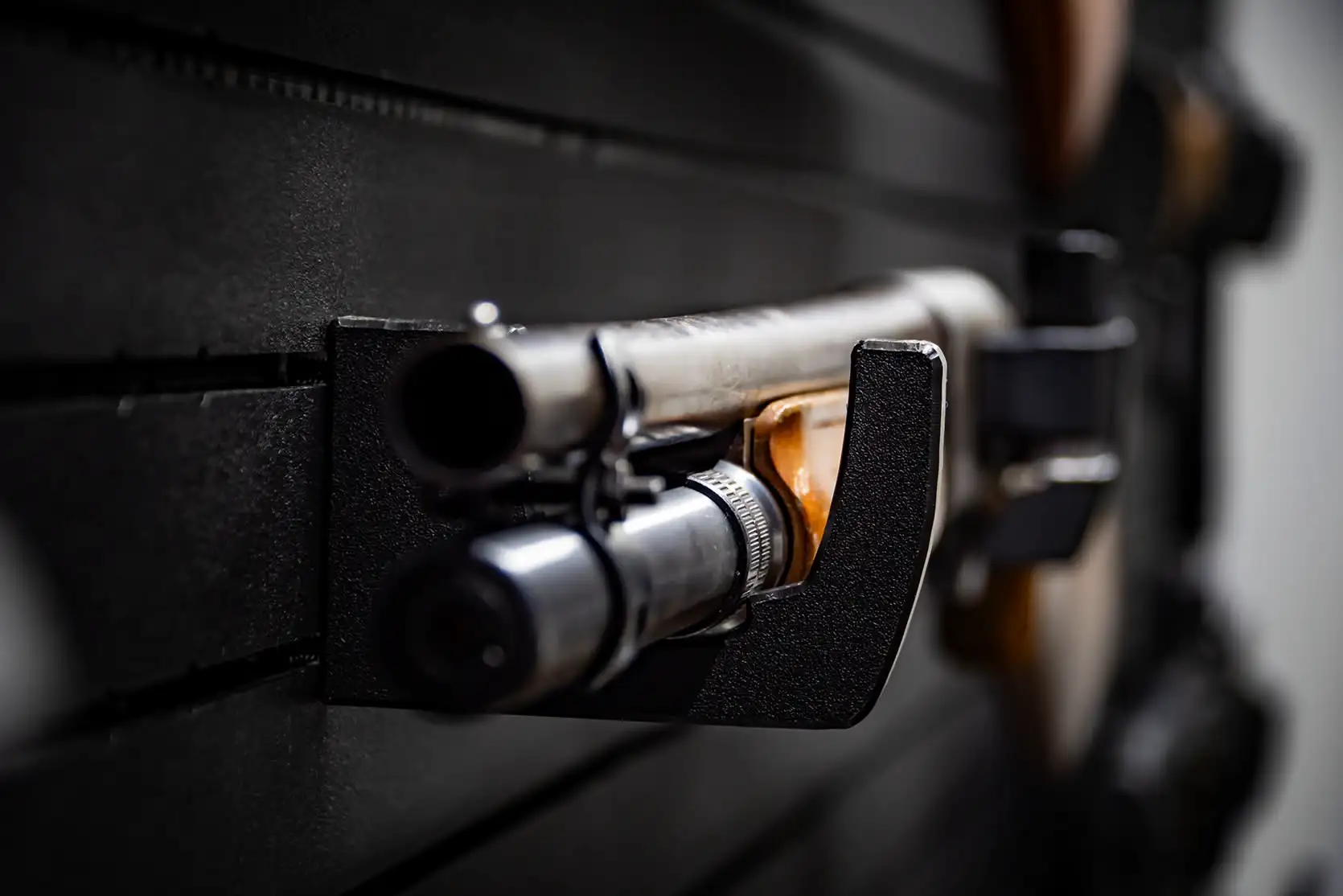 Close-up front view of a dual tactical shotgun safely held by black wall hooks.